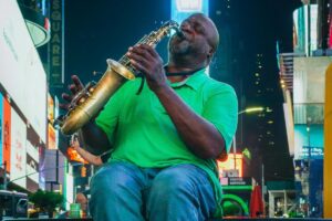 In the vibrant setting of Times Square, a musician in a green shirt passionately plays a saxophone. The surrounding bright billboards add to the energetic atmosphere. Just as this scene draws attention, About BaoLiba focuses on Connecting UK Influencers & Brands to the World 🌍, bridging the gap between talent and global opportunities.